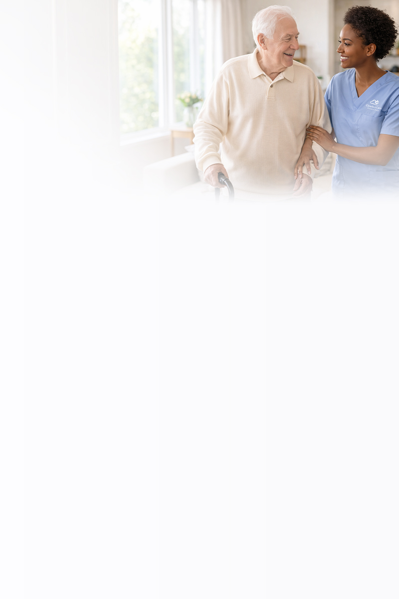 A Clouds of Care caregiver in blue scrubs assists an elderly man with a cane, both smiling as she supports him while walking at home