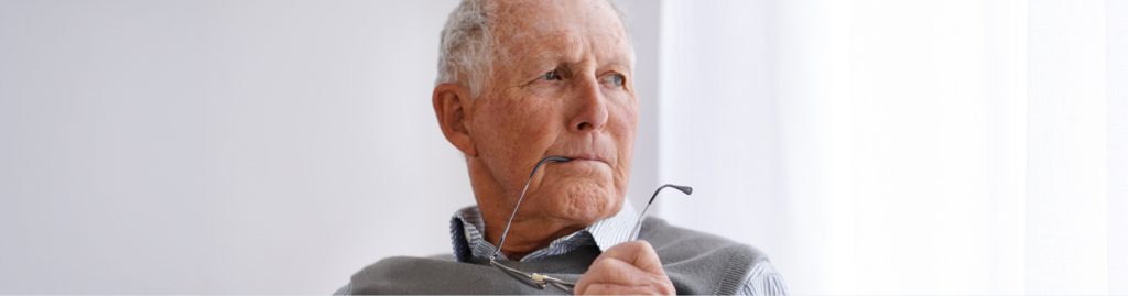 Elderly man holding glasses and gazing thoughtfully, considering in-home care options for himself or a loved one